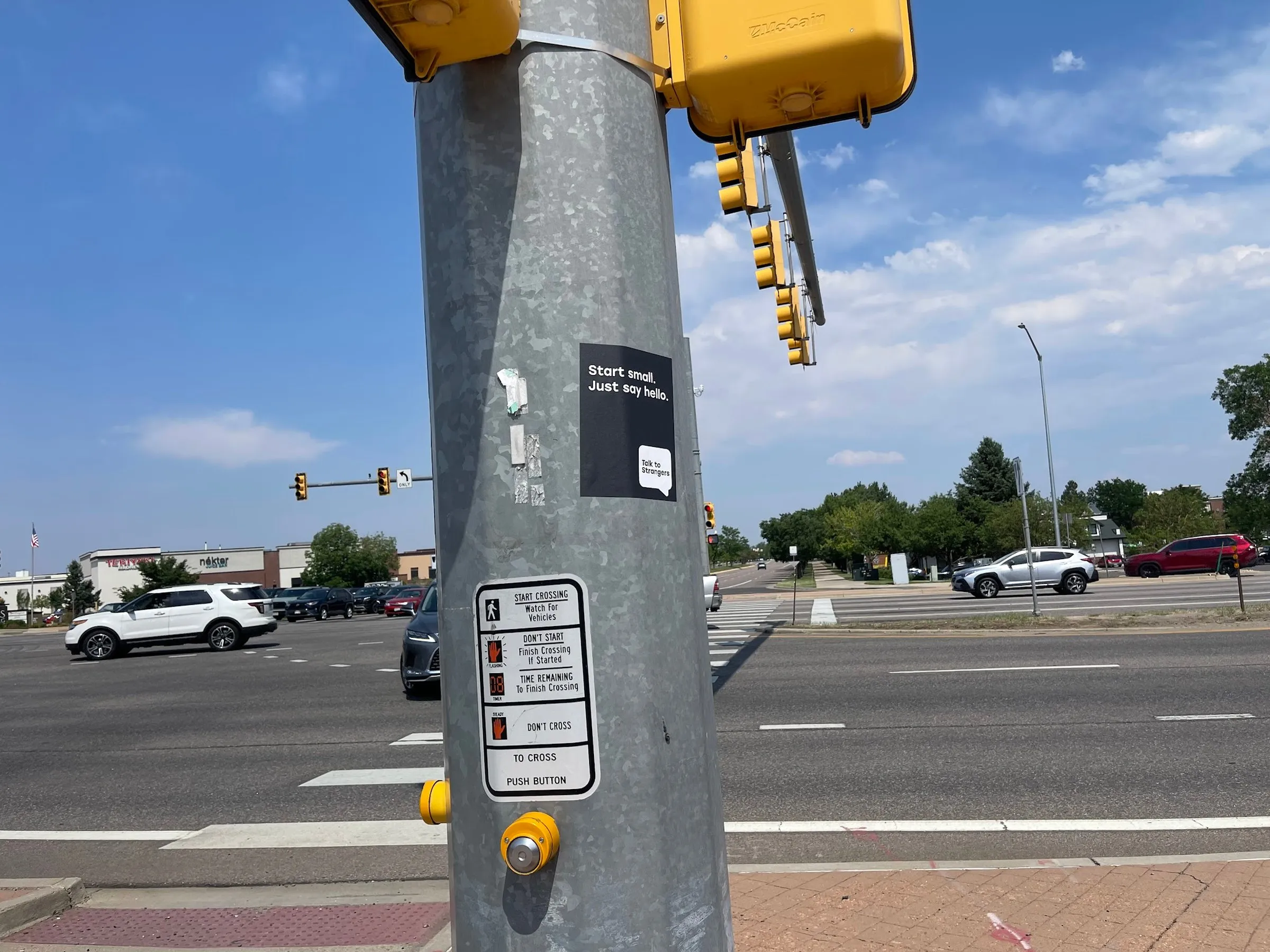 Talk to Strangers pole sticker install by Beyond Street Media at 5901 S Wadsworth Blvd, Littleton, Colorado — a pole sticker on a traffic signal pole beside a wide arterial.