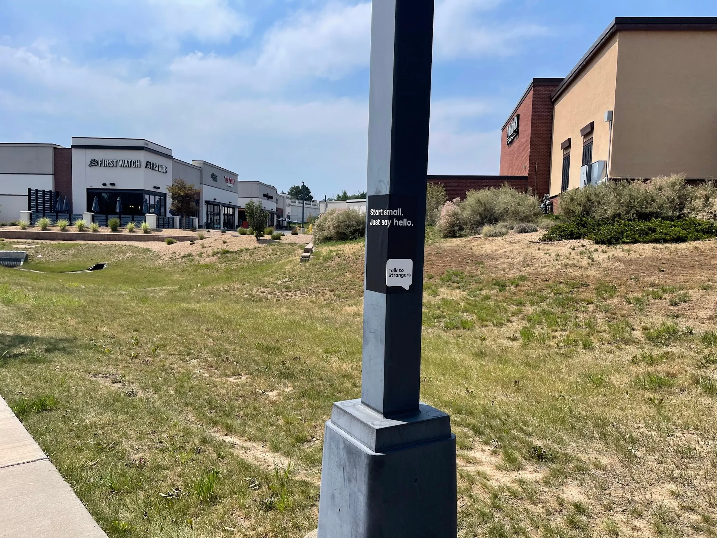 Talk to Strangers pole sticker install by Beyond Street Media at 8285 W Bowles Ave, Littleton, Colorado — a pole sticker on a pole outside a suburban retail center.