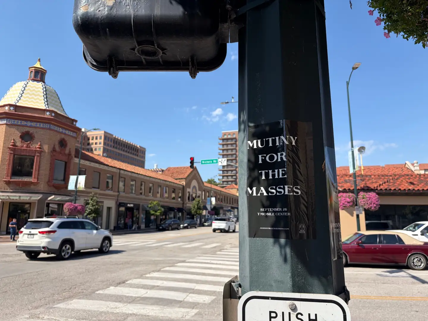 Johnny Blue Skies Mutiny for the Masses pole snipe on a dark pole at Country Club Plaza, tiled dome rooftop visible past a crosswalk