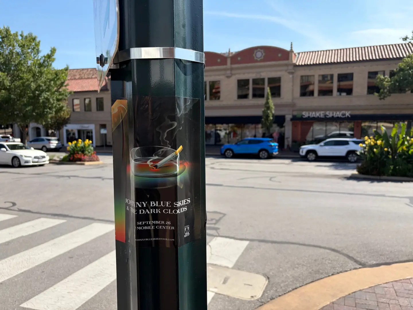 Johnny Blue Skies ashtray pole snipe at Country Club Plaza, poster near a Shake Shack storefront with a blue SUV parked across the street