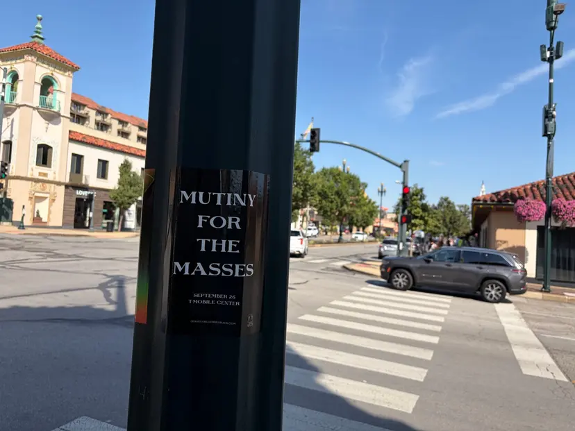 Mutiny for the Masses pole snipe at Country Club Plaza, a Spanish-tile clocktower building beyond a crosswalk and traffic signal