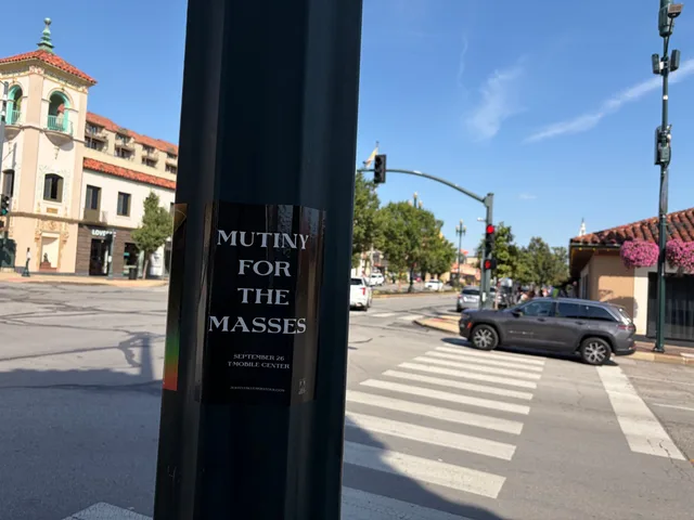 Mutiny for the Masses pole snipe at Country Club Plaza, a Spanish-tile clocktower building beyond a crosswalk and traffic signal