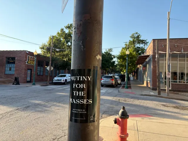 Mutiny for the Masses pole snipe on a pole at Broadway Boulevard, Westport, a red fire hydrant on the corner by a brick storefront