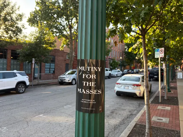 Mutiny for the Masses pole snipe on a ridged green pole at Broadway Boulevard, Westport, brick storefronts and parked cars