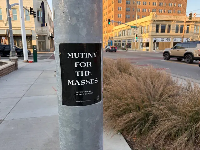 Mutiny for the Masses pole snipe on a galvanized pole at West 38th Street, Westport, tan brick storefronts glowing gold at sunset