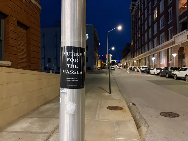 Mutiny for the Masses pole snipe on an aluminum pole at Southwest Boulevard, Crossroads, brick lofts on a quiet street at night