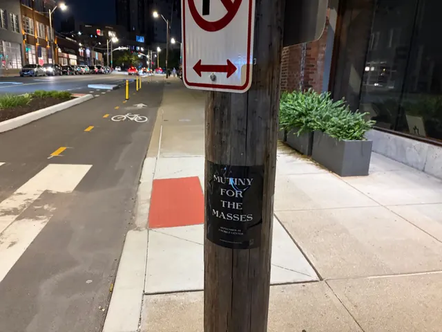 Mutiny for the Masses pole snipe on a wooden utility pole at Southwest Boulevard, Crossroads, a bike lane and no U-turn sign on the sidewalk