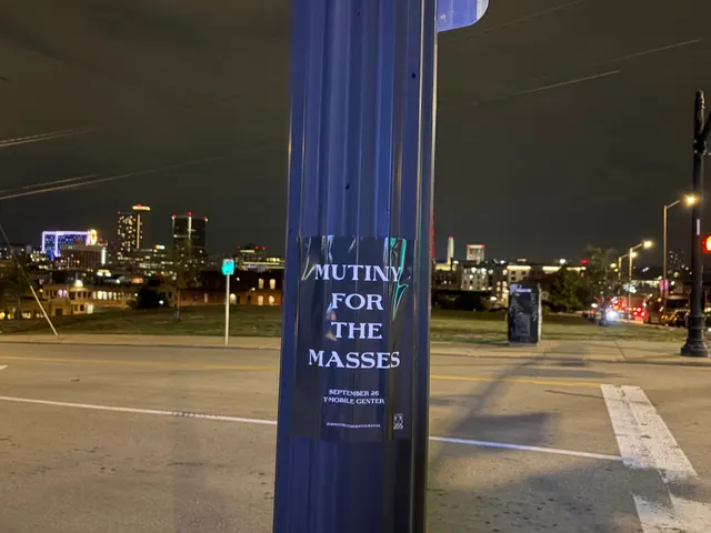 Mutiny for the Masses pole snipe on a blue pole at West 18th Street, Crossroads Arts District, the KC skyline lit at night